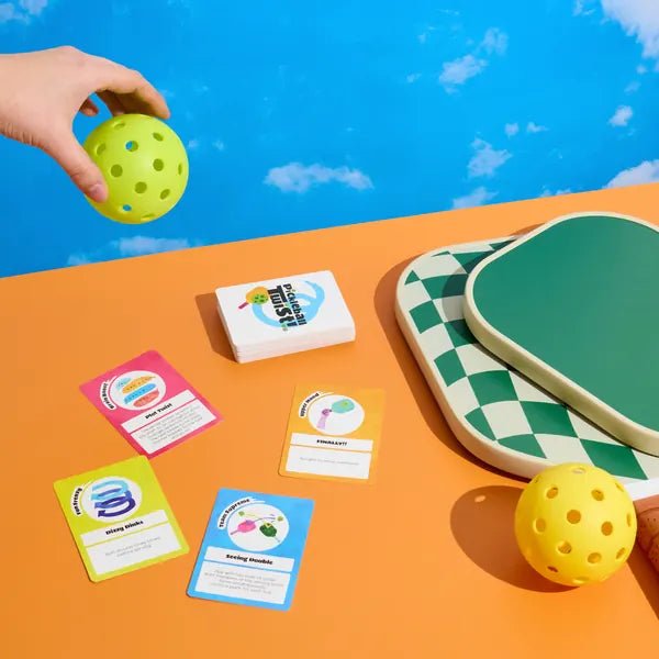 Pickleball Twist® cards, deck and paddles on a court-colored table